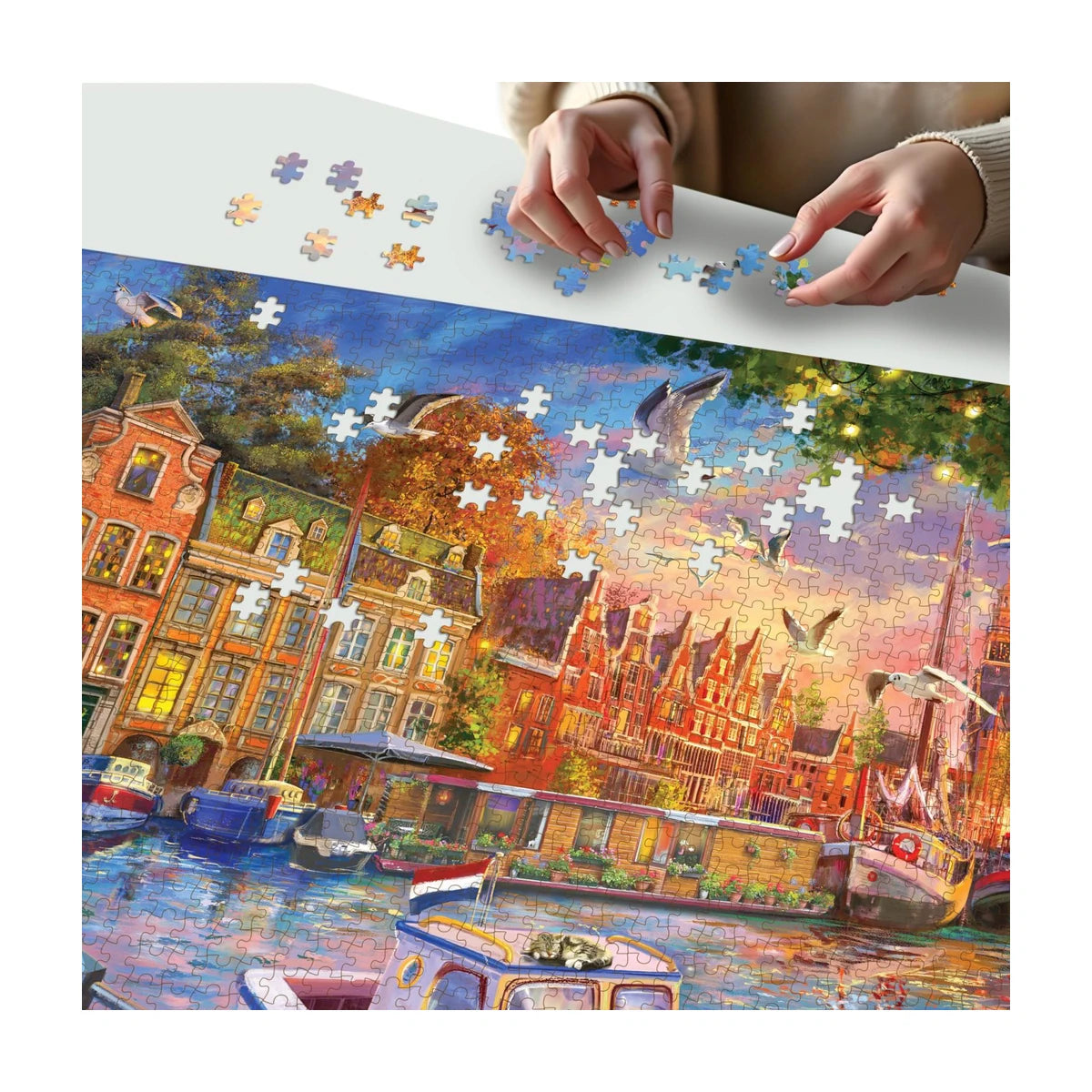Hands building the Waterfront Serenity 1500pc puzzle showing detailed harbour buildings, boats, and sunset sky pieces