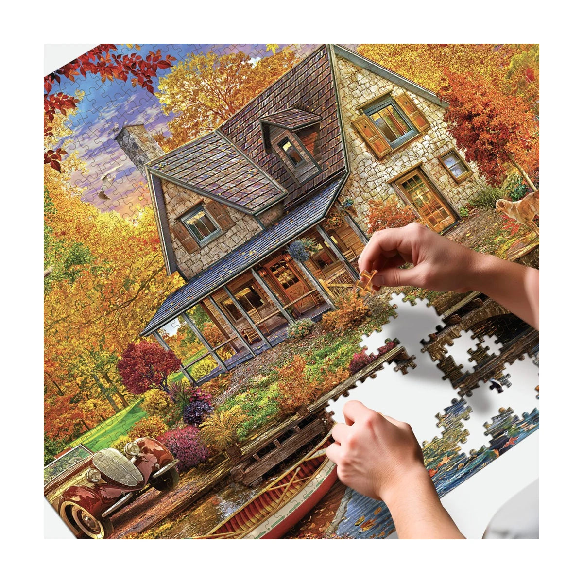 Hands placing pieces on the RGS Autumn Cottage 1500 piece puzzle in progress on a table
