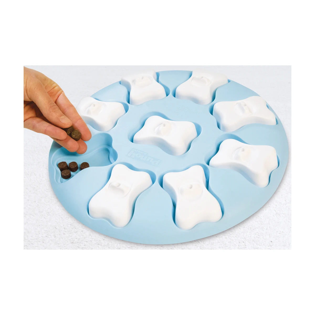 Hand placing kibble into Nina Ottosson Puppy Smart level 1 blue dog puzzle treat compartments