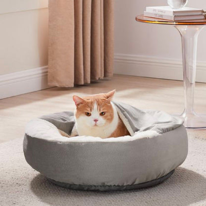 Ginger and white cat resting in a Grey Cozy Cuddler Ilan pet bed, partially tucked beneath the built-in blanket in a cosy living room.
