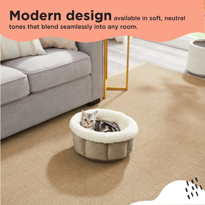 Tabby cat relaxing in a Best Friends by Sheri Cuddle Cup Ilan Mini dog and cat bed in Wheat, featuring a soft white faux fur rim and textured fabric exterior in a modern living room.