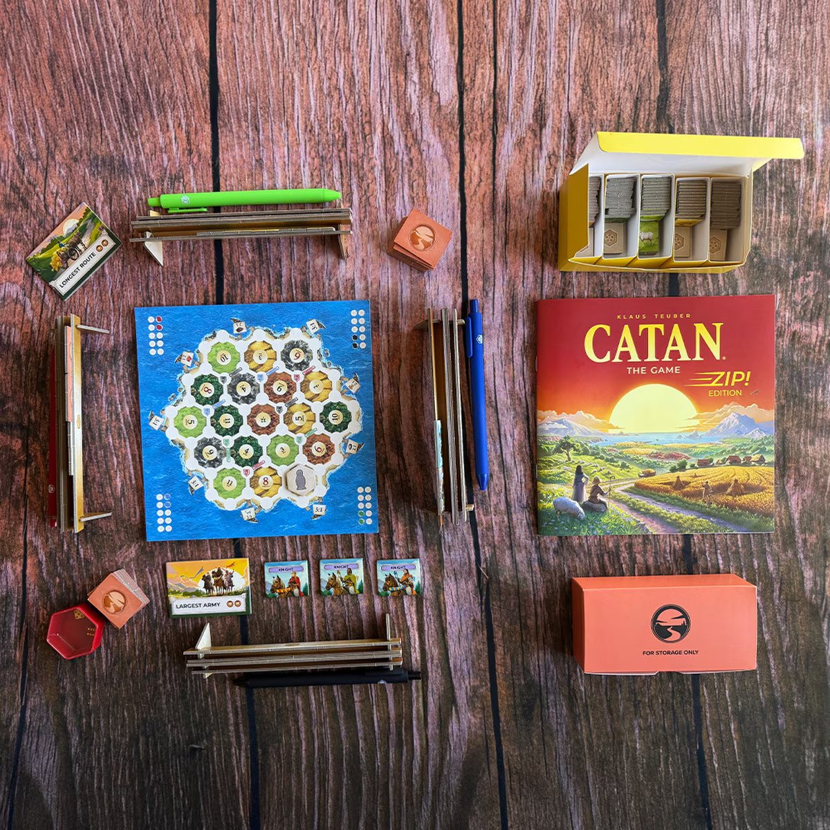 CATAN Zip Edition tabletop setup with paper map, resource tiles, pens, storage boxes and game components