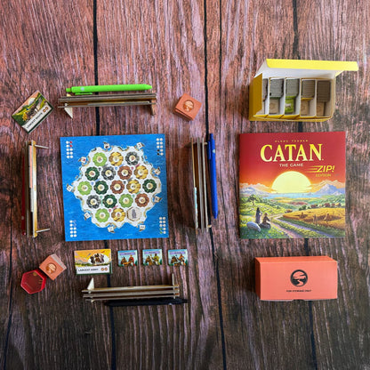 CATAN Zip Edition tabletop setup with paper map, resource tiles, pens, storage boxes and game components