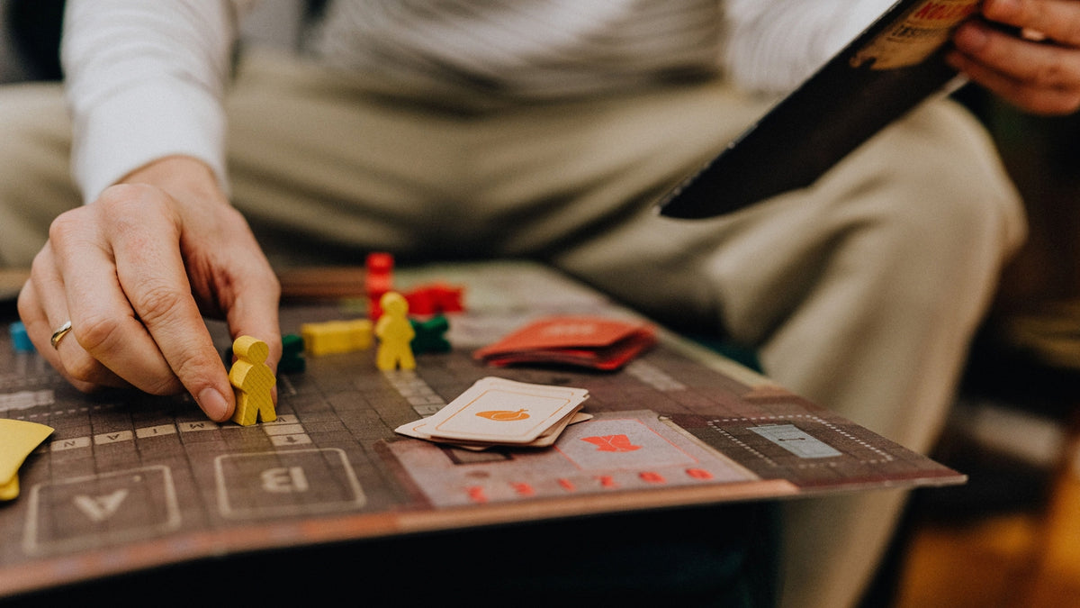 Person moving a yellow game piece on a board game with cards and colourful playing pieces