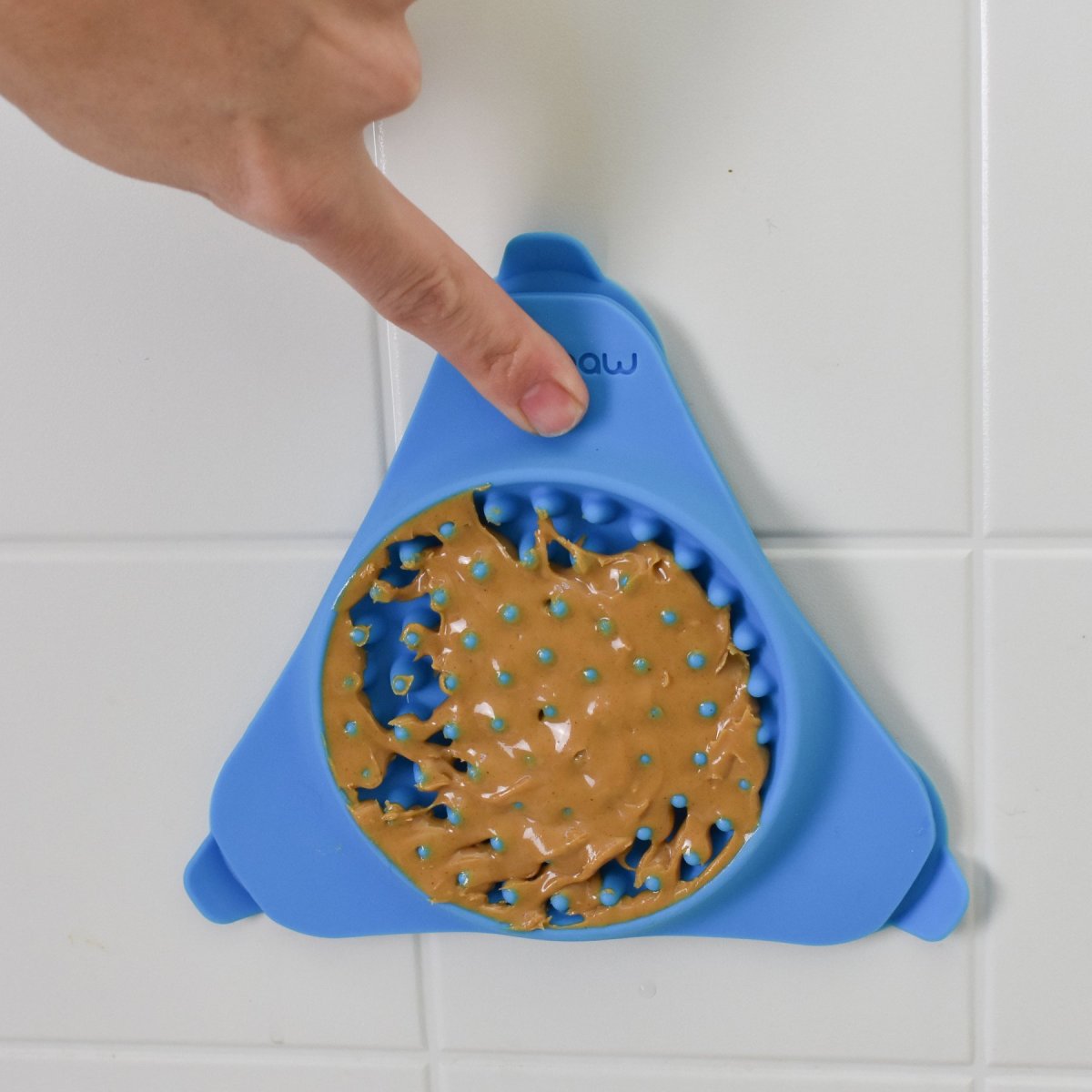 Aquapaw Slow Treater blue dog lick mat suctioned to a smooth tiled surface