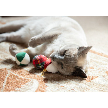 Siamese-style cat reaching its paw towards the Rosewood Festive Bauble Trio cat toys in red, green and tartan Christmas designs.