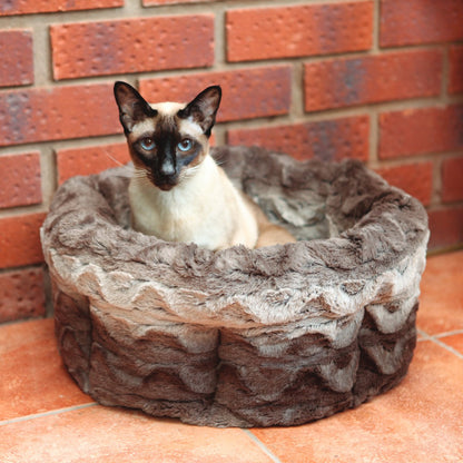 Siamese cat sitting inside the Rosewood Grey & Cream Snuggle Plush Round Cat Bed, showing its deep grey patterned plush walls and cosy cushioned design.