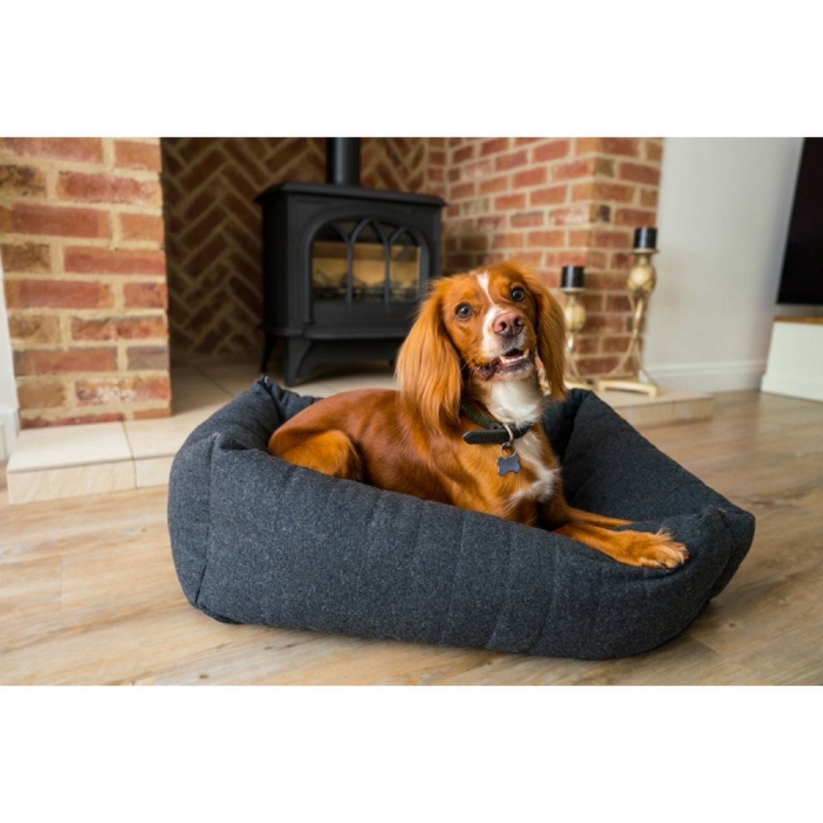 Brown and white dog relaxing in a Rosewood Grey Felt Memory Foam Square Dog Bed with padded sides, positioned in a living room beside a brick fireplace.