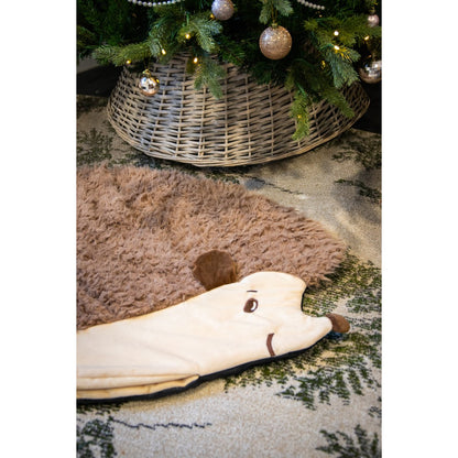 Rosewood Hedgehog Snuffle & Burrow Blanket spread out on a patterned rug beneath a decorated Christmas tree, showing its cream hedgehog face and brown fluffy body.