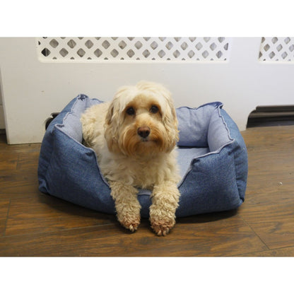 Cream-coloured dog resting in the blue Rosewood Luxury Cooling Pet Bed 60 cm with its front paws hanging over the lowered front edge on a wooden floor.