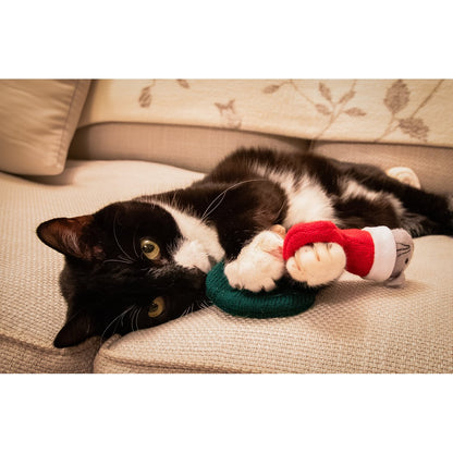 Black and white cat lying on a beige sofa and holding the green stocking from the Rosewood Martha & Mayor Mice Duo Christmas cat toys.