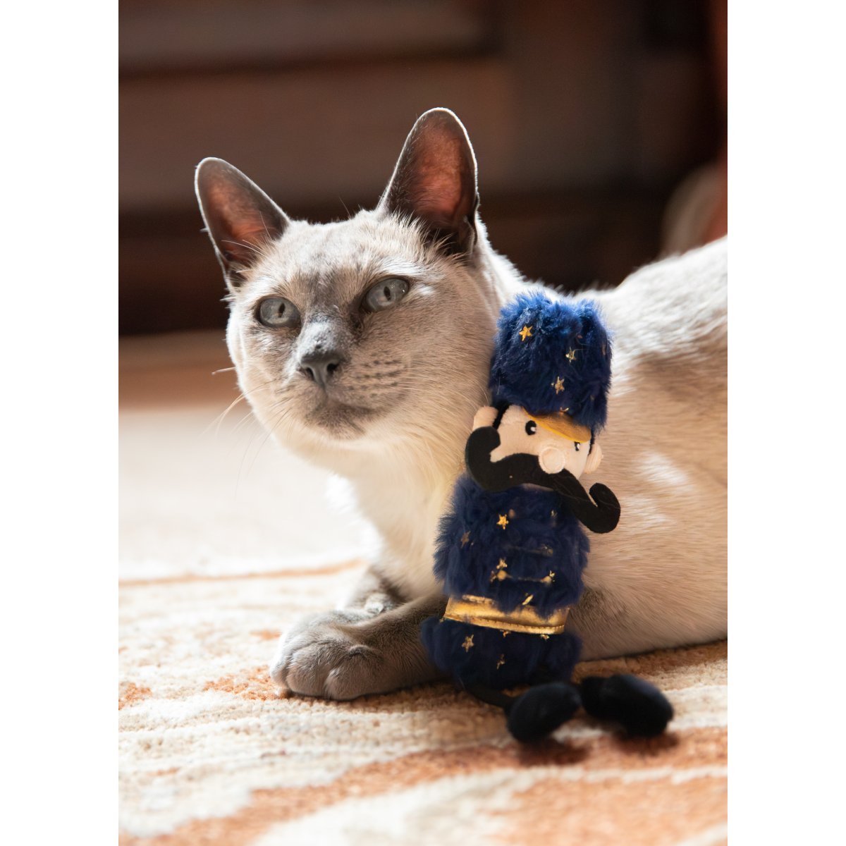 Siamese-style cat resting beside the Rosewood Ned Nutcracker Christmas catnip toy, featuring a navy blue plush outfit with gold stars and black bungee legs.