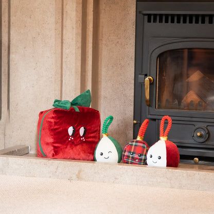 Rosewood Peter Present red plush Christmas dog toy displayed beside three festive bauble dog toys near a fireplace.