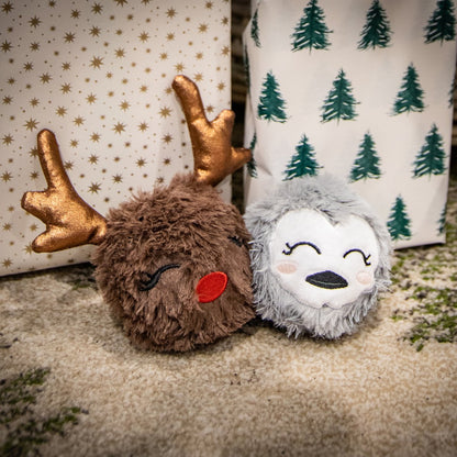 Rosewood Ralphie Reindeer and Parker Penguin plush tennis ball dog toys sitting beside wrapped Christmas presents.