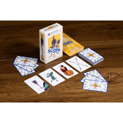 Scopa card game table setup showing illustrated cards, box and rulebook on a wooden table